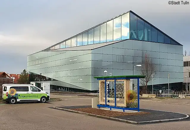 Außenansicht modernes Gebäude mit verspiegelter Fassade und vorgelagertem Parkplatz mit E-Tankstelle